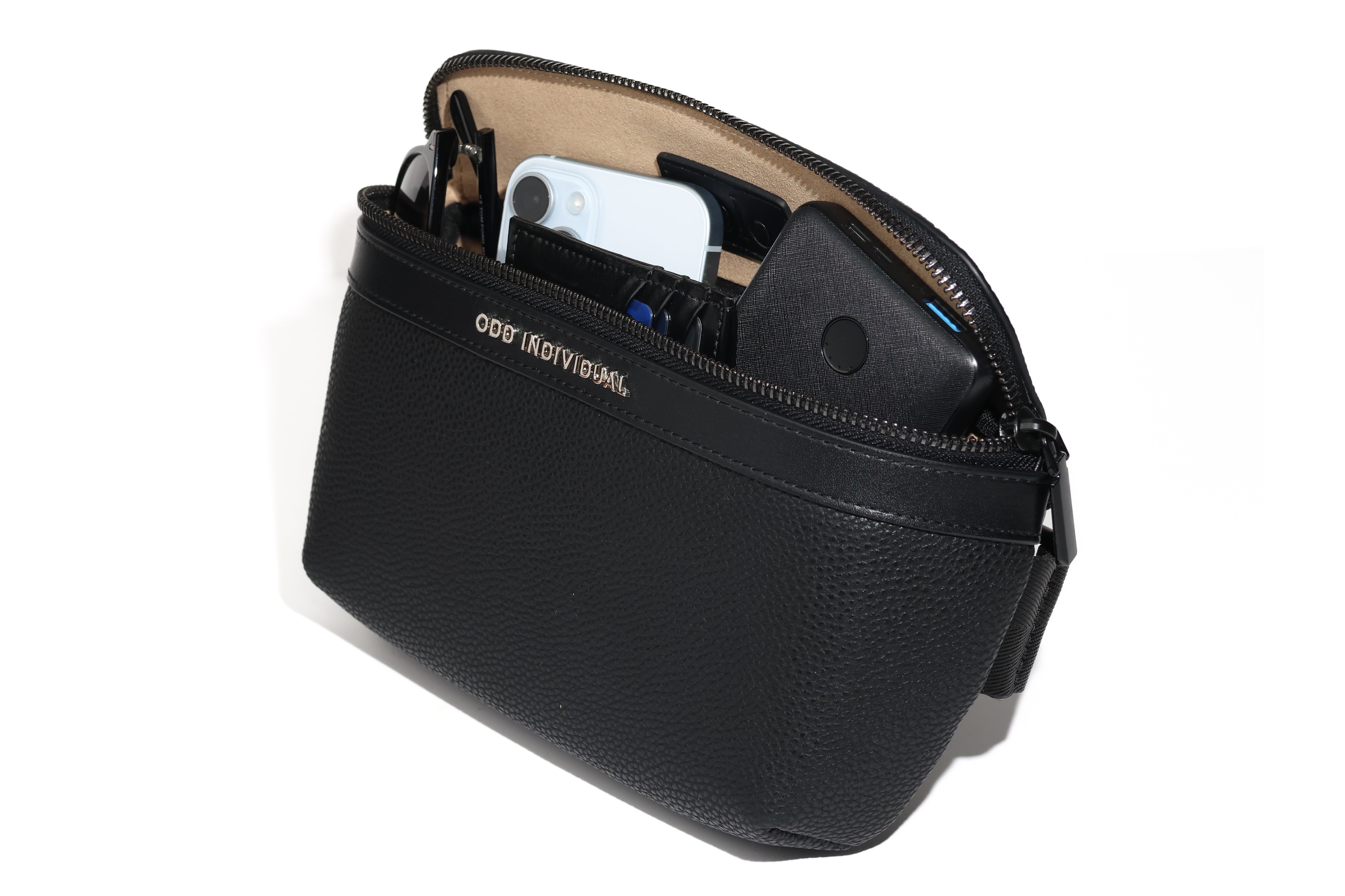 Black leather sling bag/black leather belt bag/black leather crossbody bag/black leather waist bag/black leather travel pouch with brand name 'ODD INDIVIDUAL'  with sunglasses, phone, wallet, and portable battery charger sticking out of an open zipper.